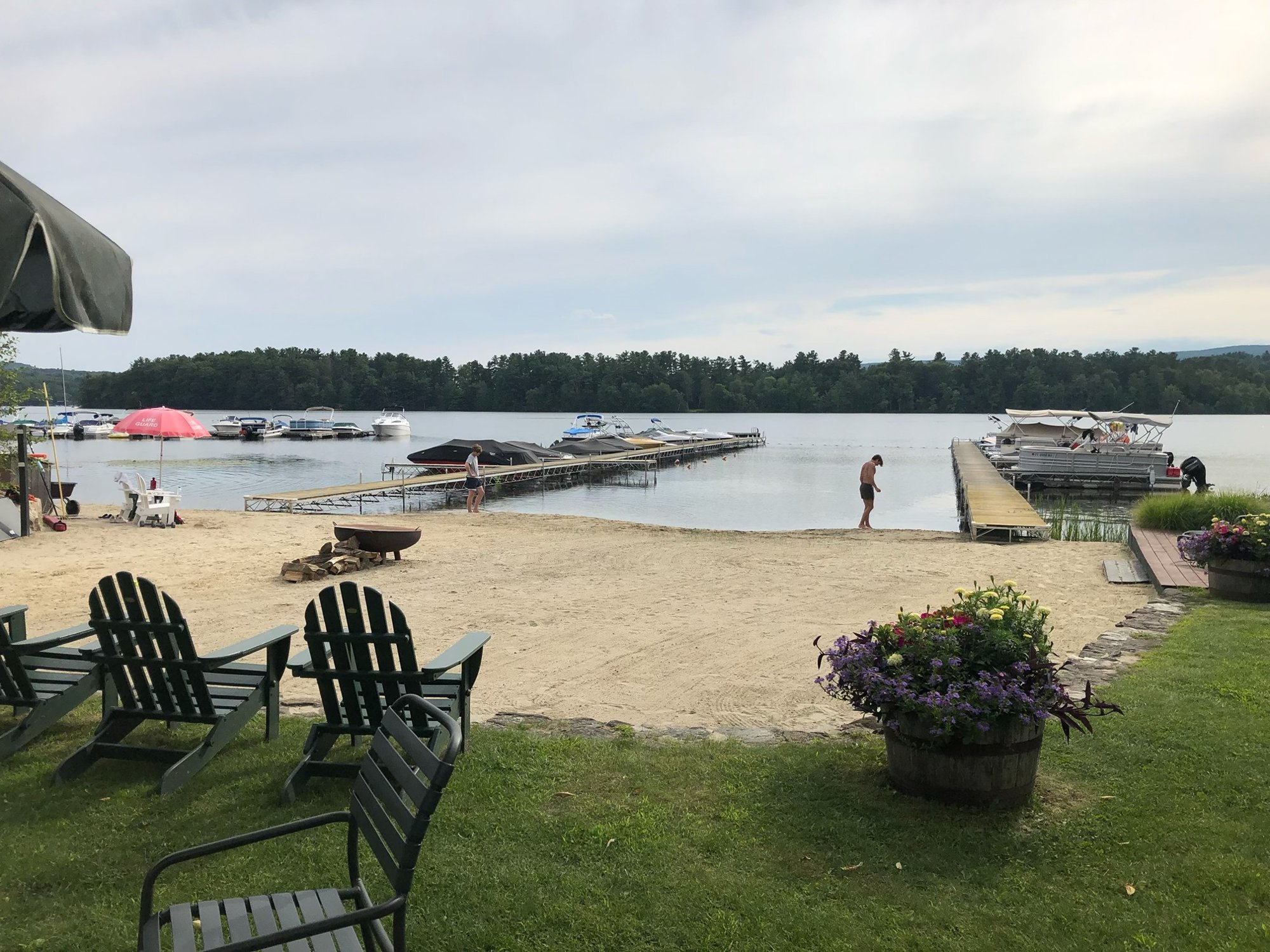 beach-2026 The club beach from the lawn: Adirondack chairs, sand, the docks and boats on the lake